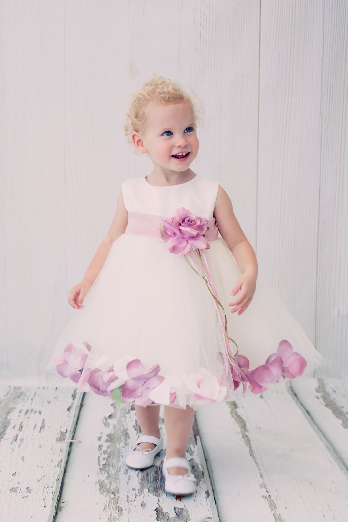 White satin flower petal baby dress with organza sash by Kid's Dream, featuring delicate floral details and a soft, elegant design.