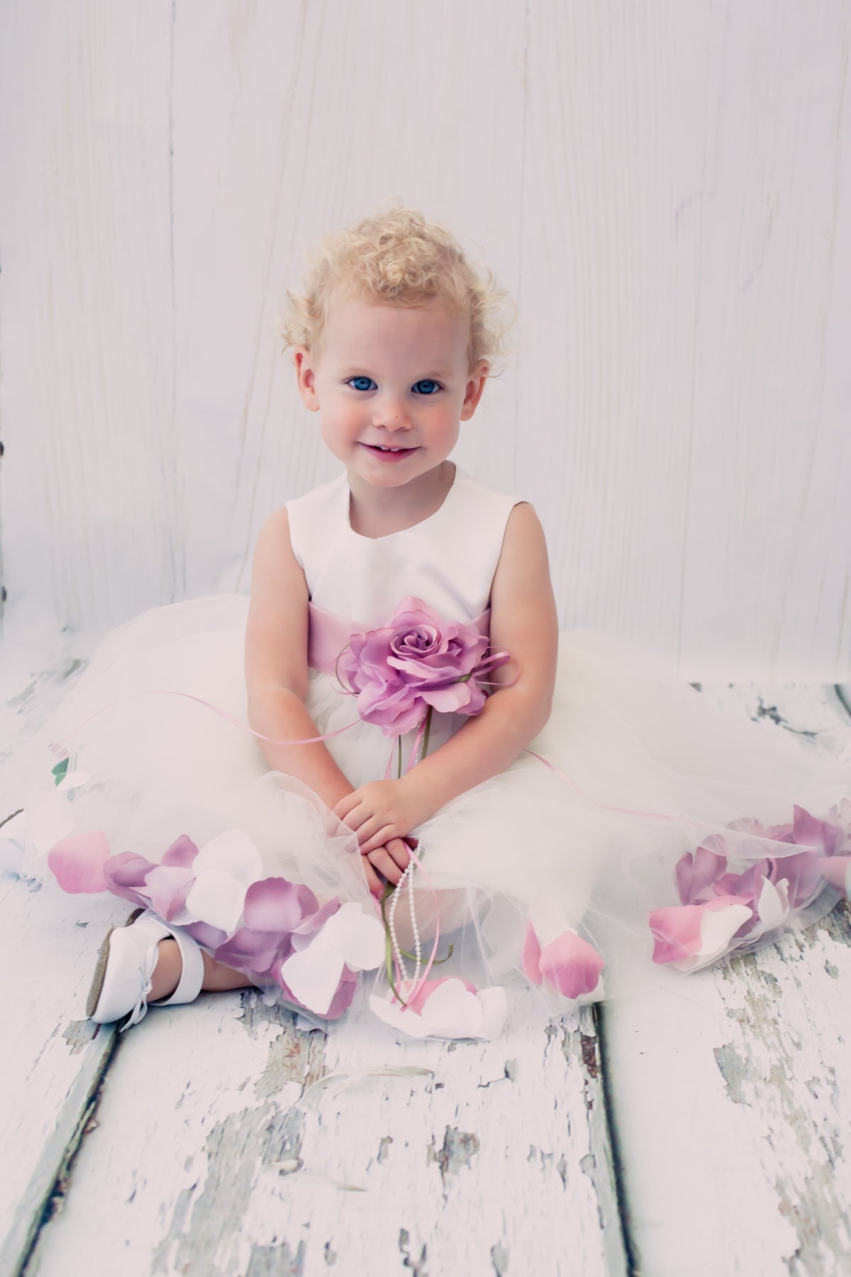 White satin flower petal baby dress with organza sash, featuring delicate floral details and a soft, elegant design for infants.